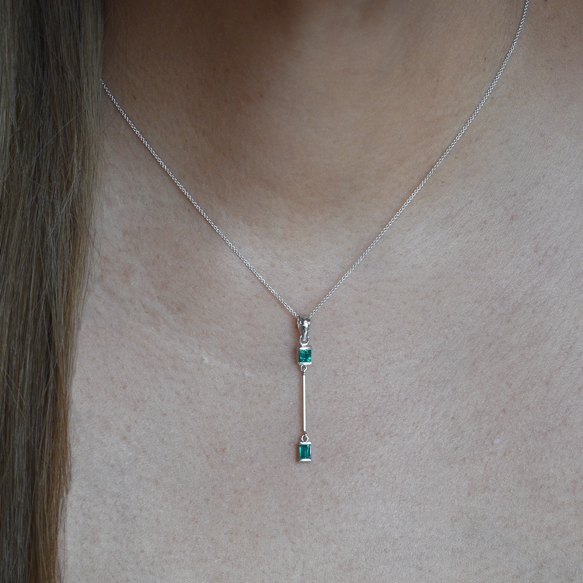 Thin emerald necklace on models neck with small emerald cut emeralds in a delicate half bezel setting