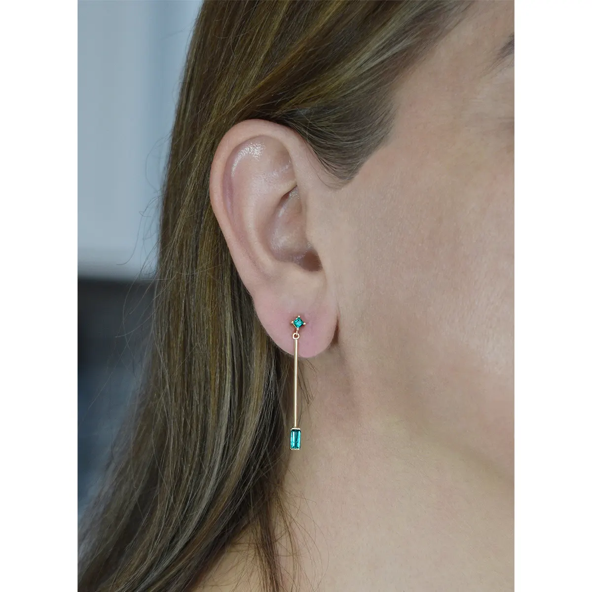 These dangle earrings have 2 small square-cut emeralds set in prongs at the top and 2 long and thing baguette cut emeralds set at the bottom of each earring in half bezels